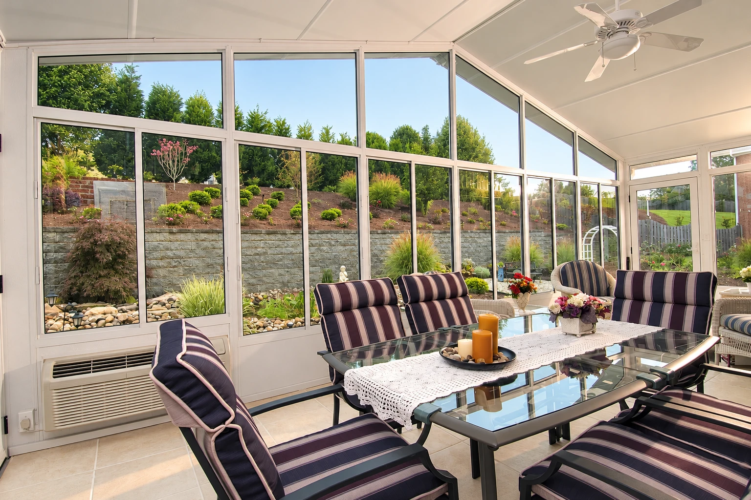 Four-season sunroom with large windows, ceiling fan, and striped lounge chairs around a glass dining table.