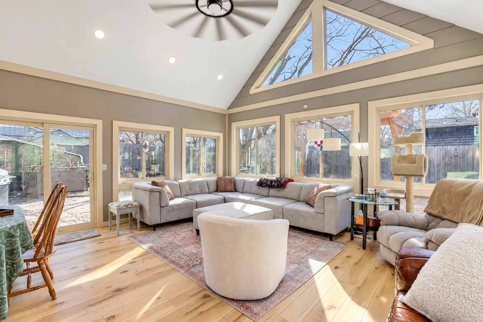 Bright sunroom living area with vaulted ceiling, triangular clerestory windows, and a large sectional sofa.